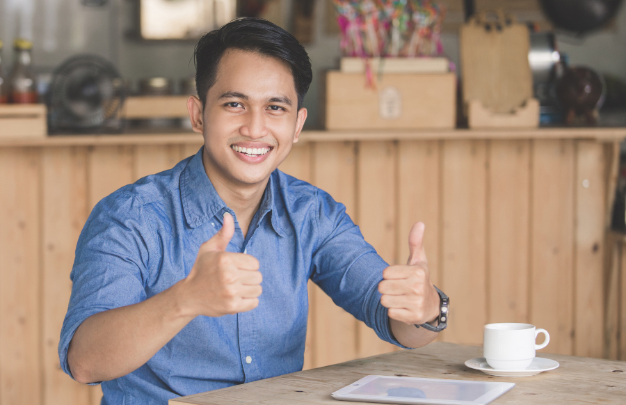 shot of young male showing thumbs up while sitting in a cafe 