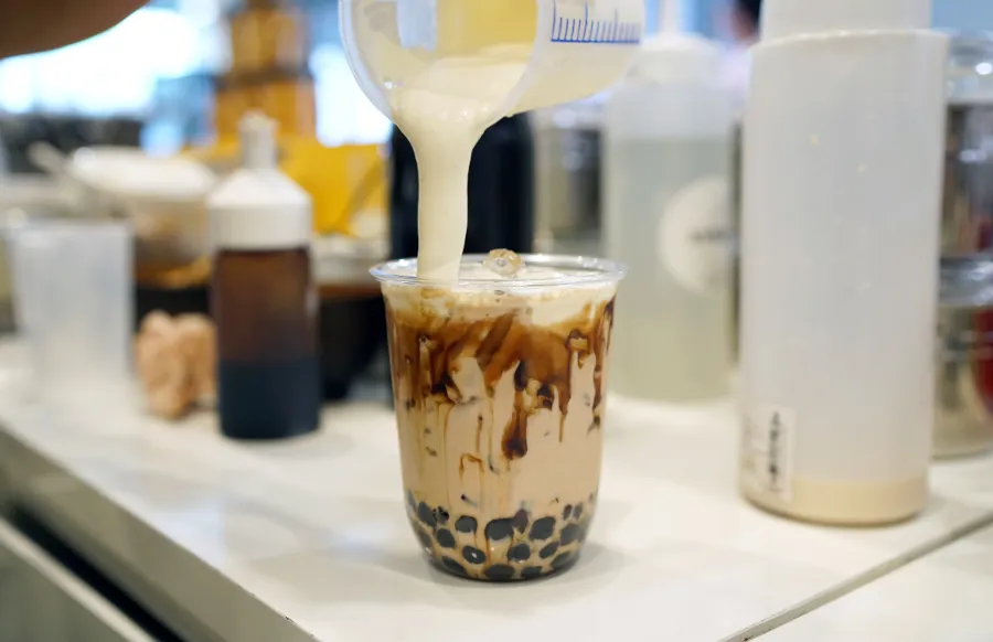 Bubble Milk Tea - pouring cream cheese into glass of milk tea with black sugar syrup and hot black pearl 